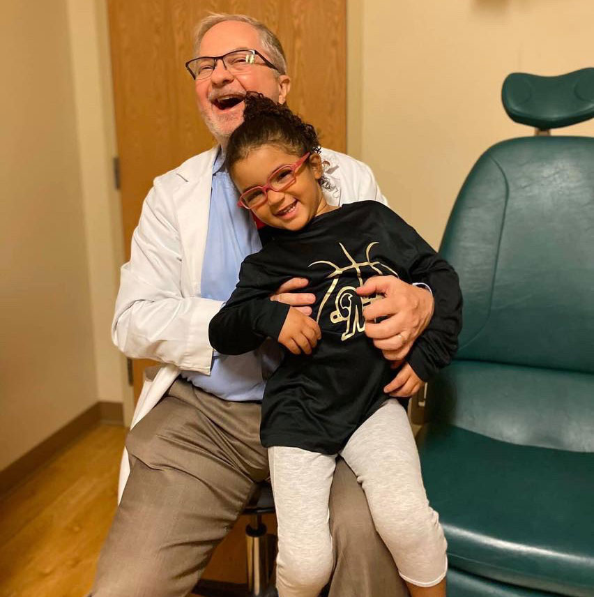 A doctor holding a child and both are lauging.